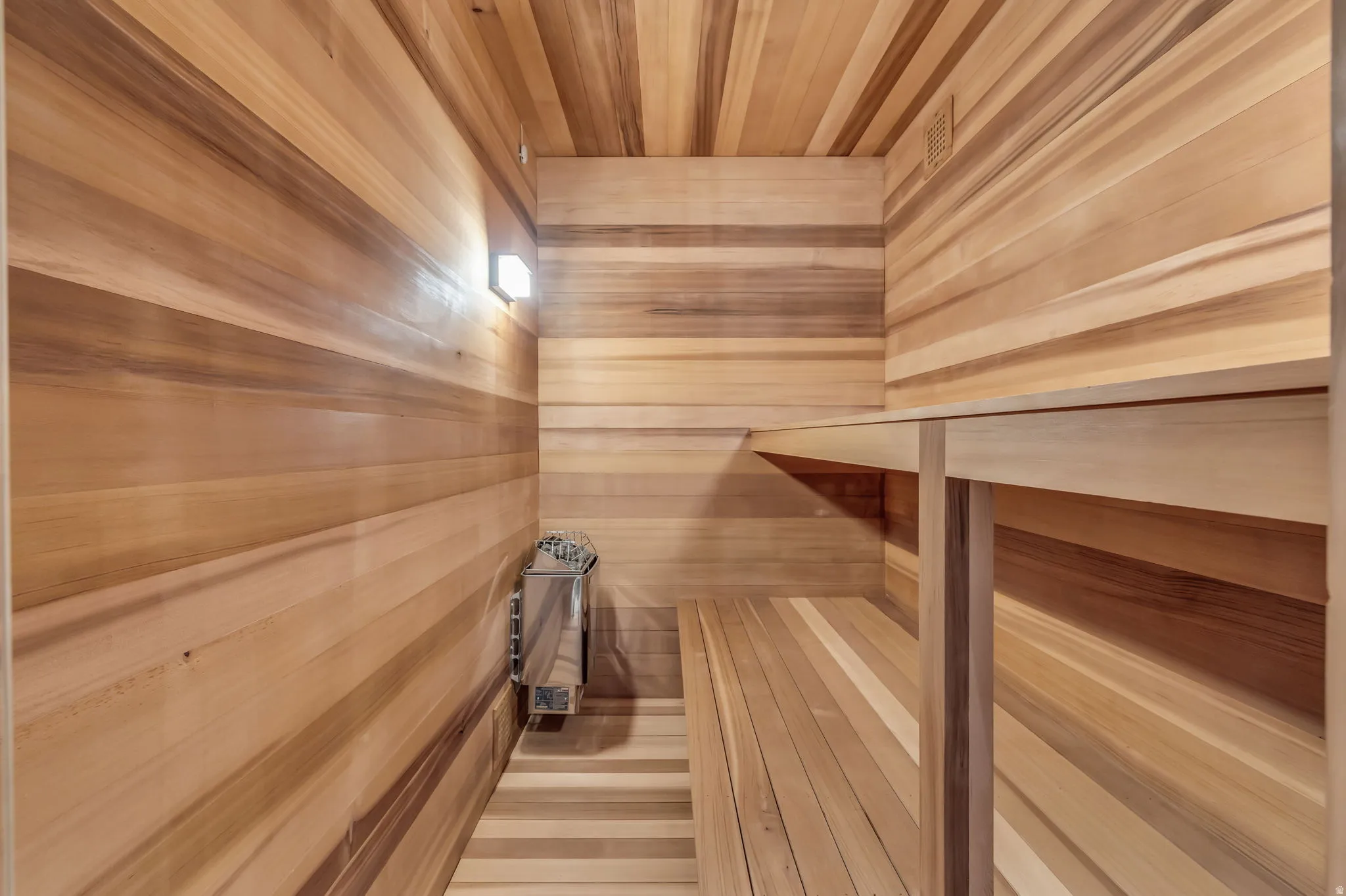Wood-paneled sauna featuring a built-in heater, integrated bench seating, and overhead ventilation