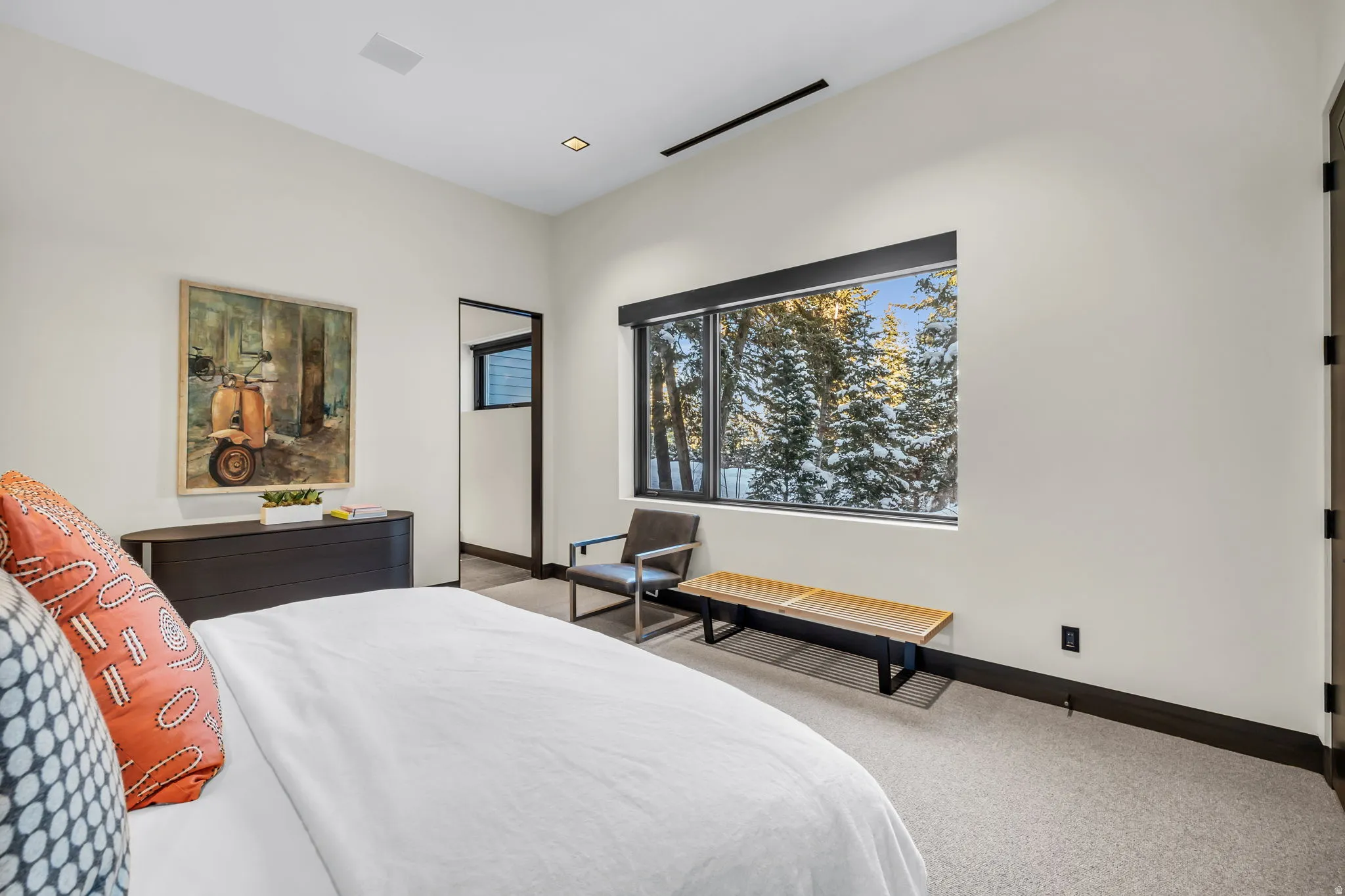 Spacious room featuring a large window with exterior winter scenery, light-toned carpeting, dark baseboards, and recessed lighting