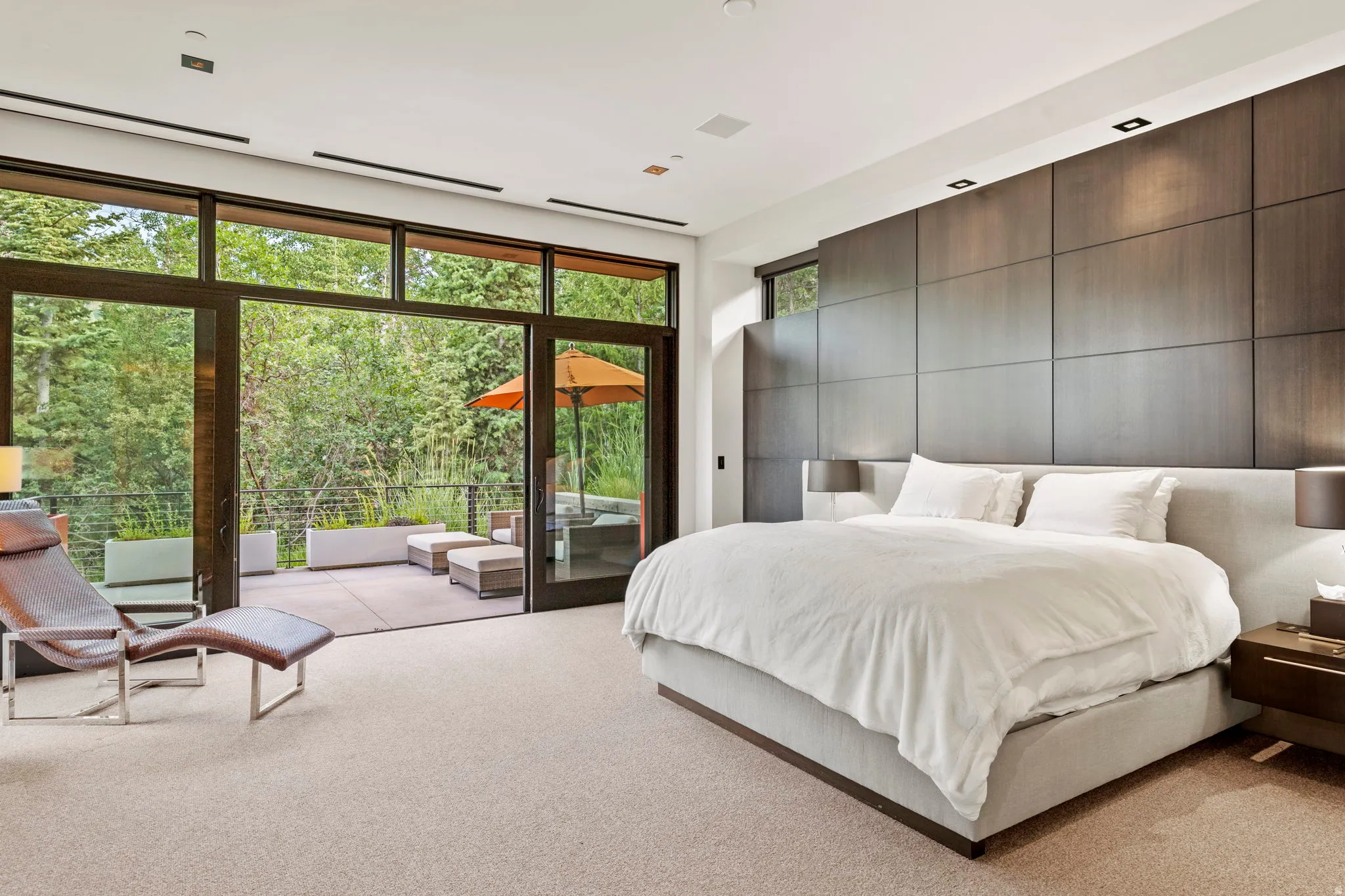 Expansive bedroom featuring a floor-to-ceiling glass wall with sliding doors leading to an outdoor patio