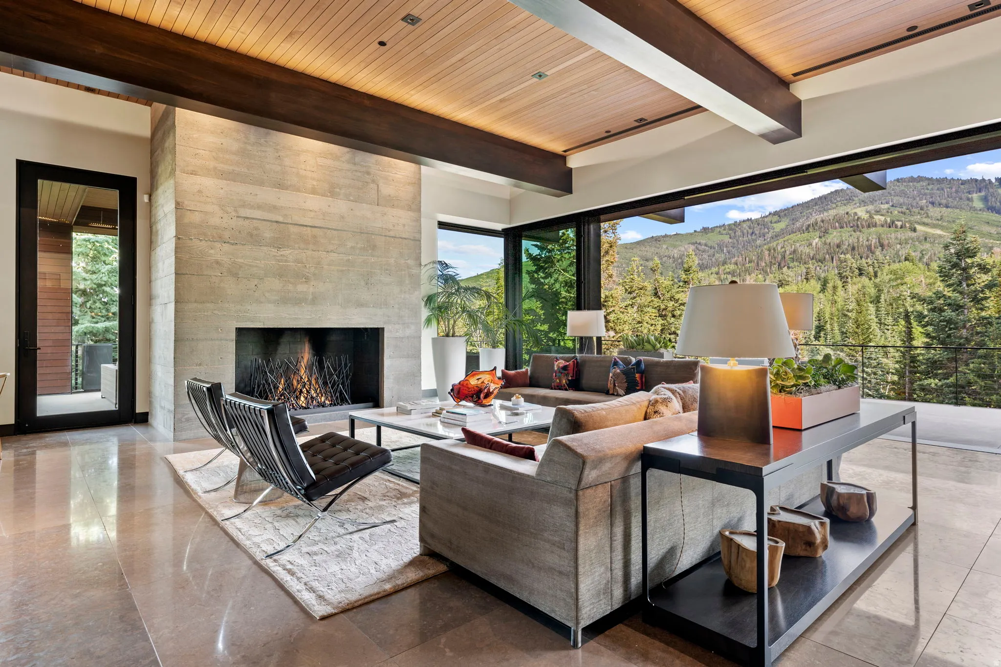 Spacious living area featuring a board-formed concrete fireplace, a wood-paneled ceiling with dark wood beams, and large format polished tile flooring