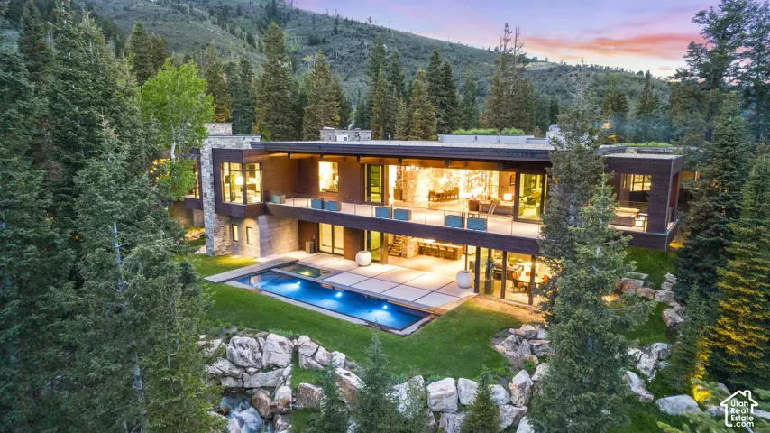 Modern architectural residence featuring extensive glass facades, multiple outdoor balconies, a rectangular swimming pool, and a structured outdoor patio space