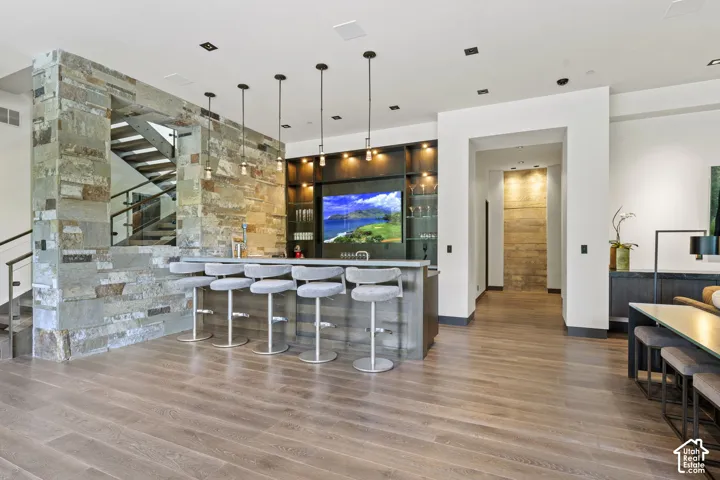 Built-in bar with pendant lighting, stone accents, and wood-finish flooring