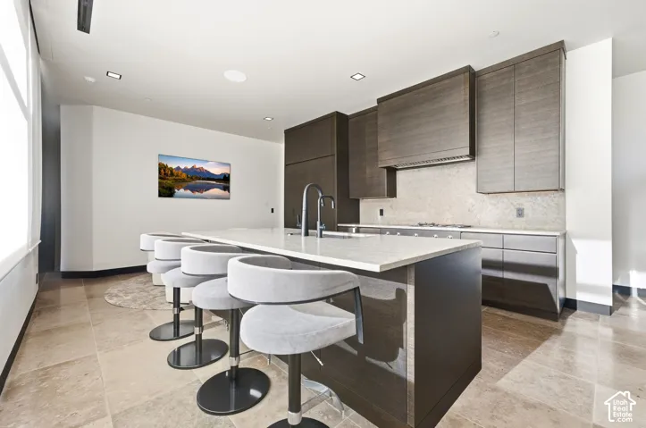 Kitchen featuring an oversized island with a light-toned countertop, built-in sink, and dark wood-finish cabinetry