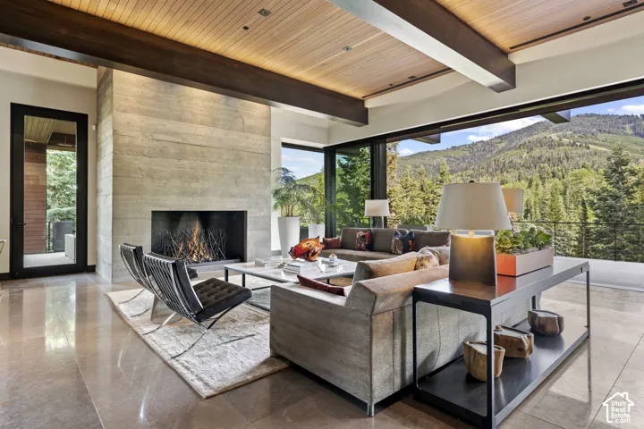 Spacious living area featuring a board-formed concrete fireplace, a wood-paneled ceiling with dark wood beams, and large format polished tile flooring