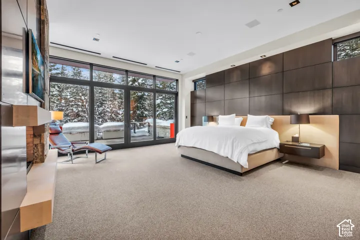 Floor-to-ceiling windows with dark frames, a built-in stone fireplace feature, dark wood paneling, and a light-toned carpet