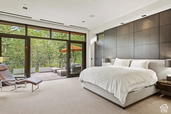 Expansive bedroom featuring a floor-to-ceiling glass wall with sliding doors leading to an outdoor patio