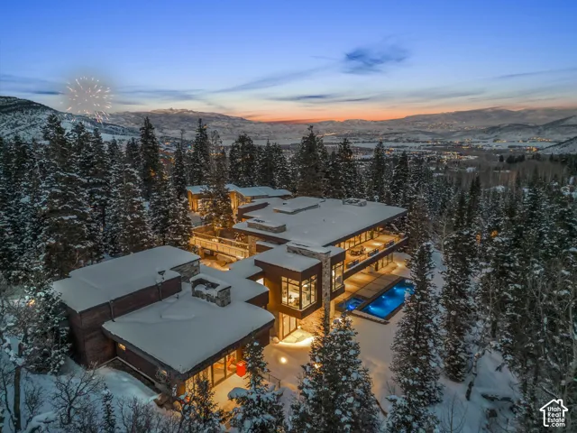 Expansive architectural residence featuring multiple outdoor terraces, large format windows, a stone exterior, and an illuminated outdoor pool