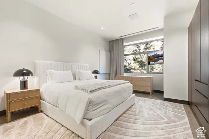 White walls, wood-finish flooring, built-in cabinetry, recessed lighting, and a large window with privacy curtains