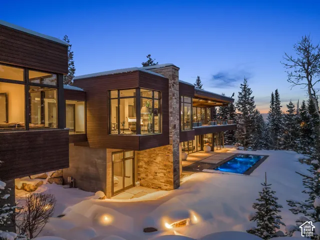 Modern exterior featuring rich wood paneling, extensive window walls, a stone pillar accent, an outdoor swimming pool, and a spacious patio area