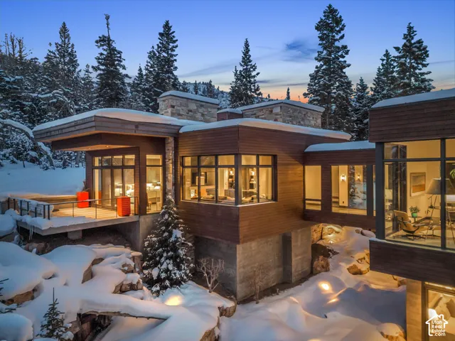 Modern mountain residence featuring extensive window walls, multi-level wood-clad exteriors, stone masonry accents, a suspended walkway, and a concrete foundational base