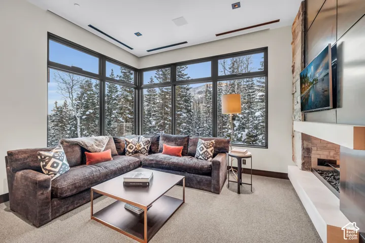 Spacious living area featuring extensive window walls, a linear fireplace with stone surround, a floating mantel, and high ceilings with recessed lighting