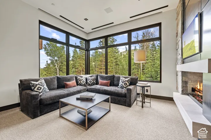 Floor-to-ceiling windows, a stone-clad fireplace with a hearth, recessed ceiling lighting, and dark trim details
