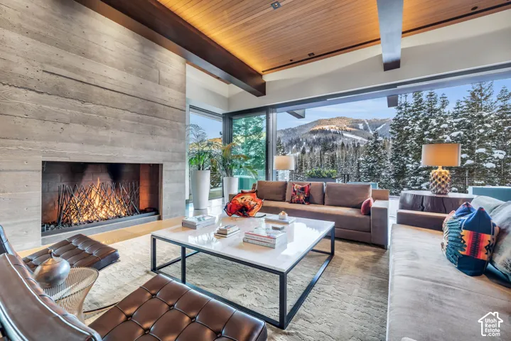 Living area featuring a board-formed concrete fireplace, full-height sliding glass doors, a wood-paneled ceiling, and exposed structural beams