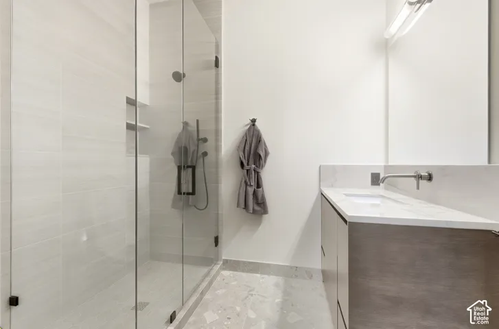 Glass-enclosed shower with tile surround and built-in shelving, complemented by a vanity with a white countertop, under-mount sink, and wall-mounted faucet