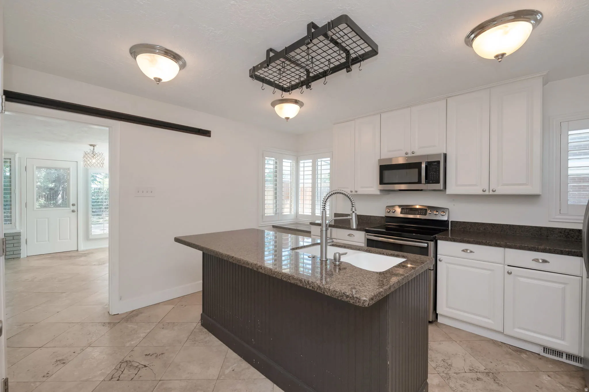 Kitchen featuring a central island with a built-in sink, white cabinetry with silver hardware, granite-look countertops, and stainless steel appliances