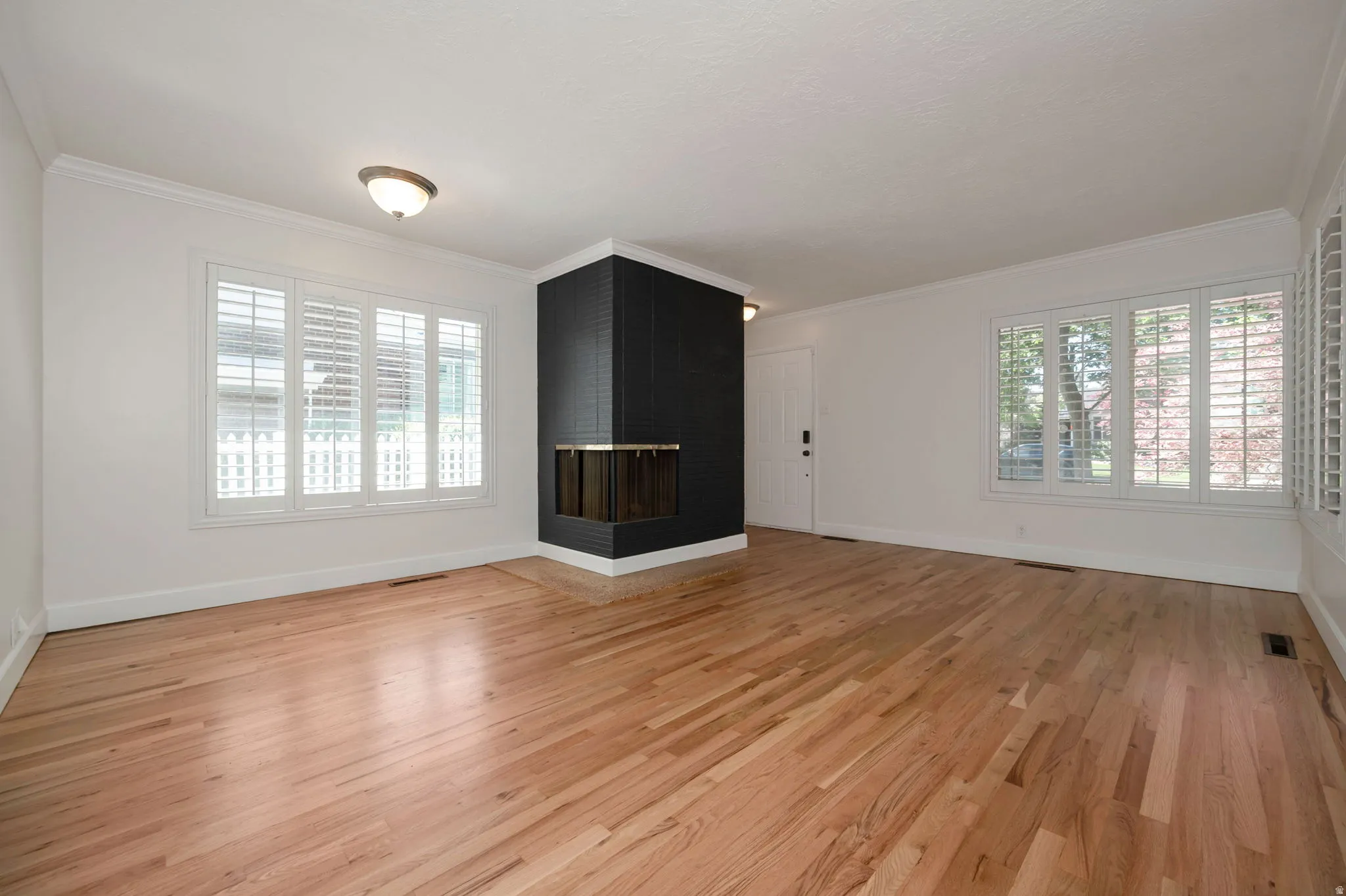 Spacious room featuring wood-finish flooring, a corner fireplace, and multiple windows with white plantation shutters