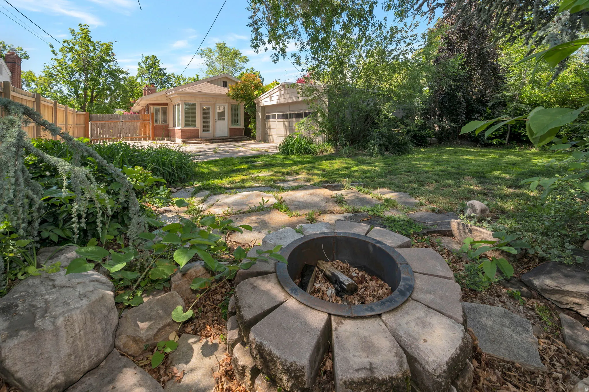 Expansive backyard featuring a stone-lined fire pit, natural stone paving, mature landscaping, and privacy fencing