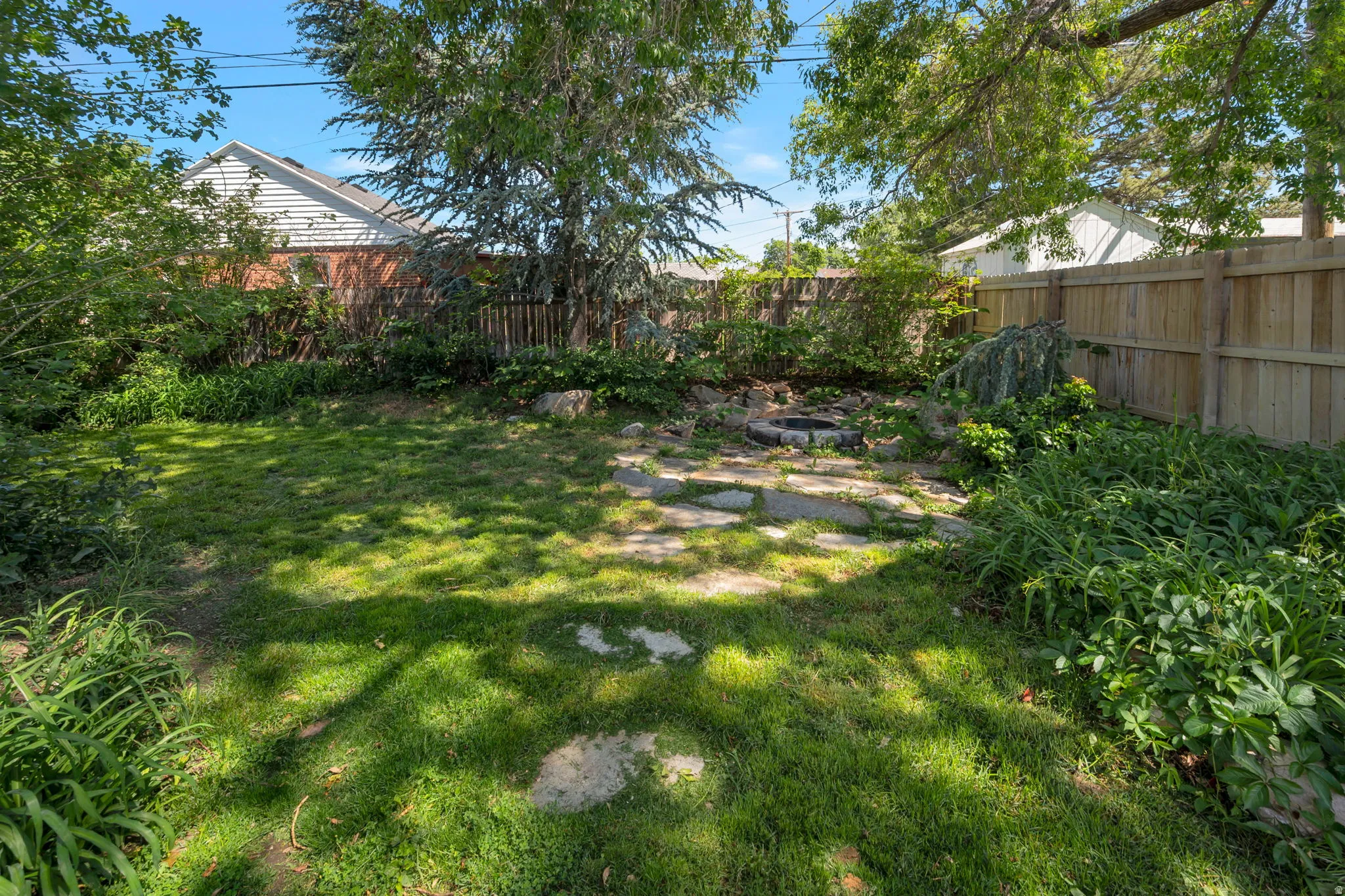 Grassy backyard area featuring a partial stone path, mature trees, and privacy fencing