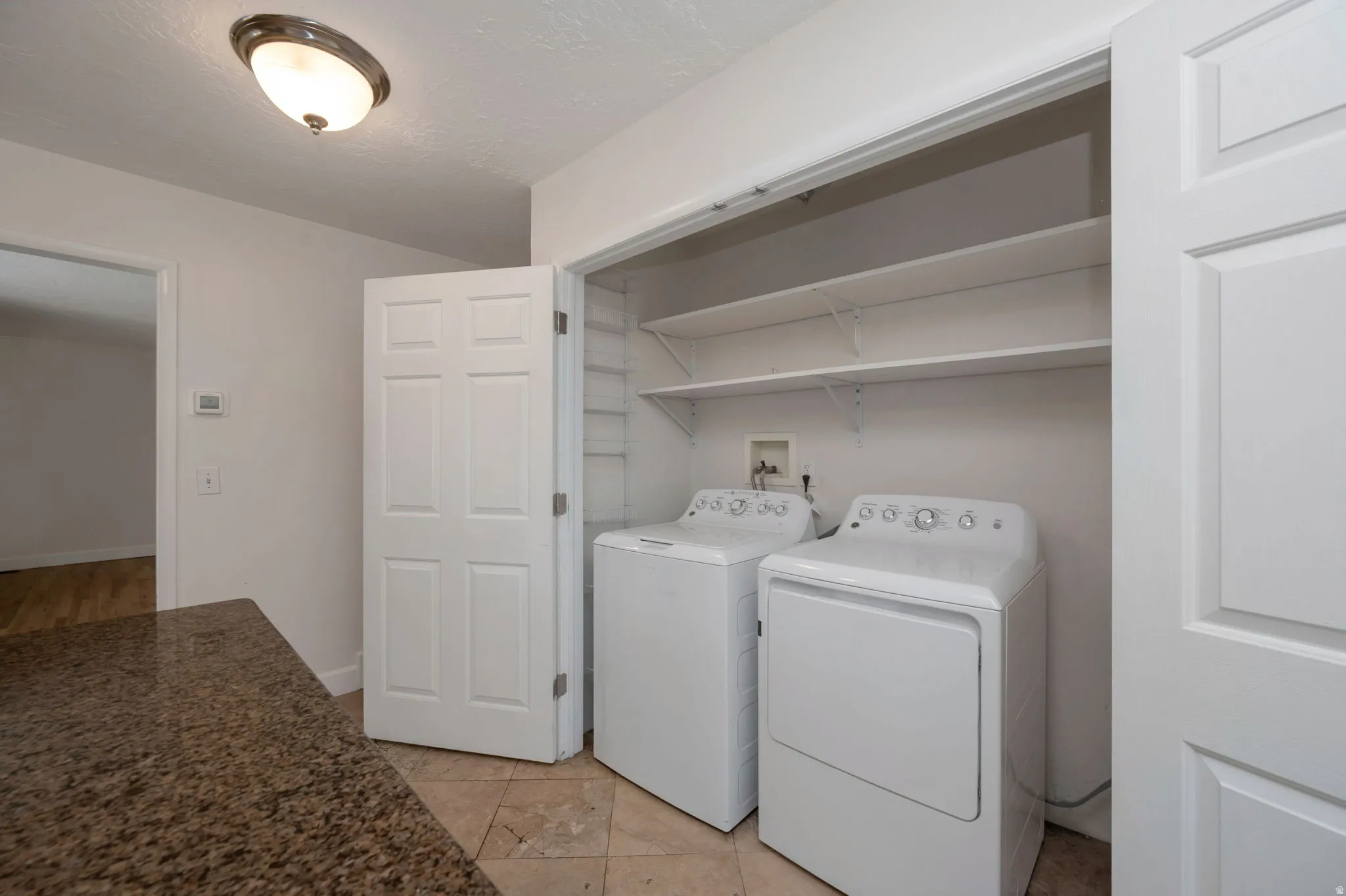 Dedicated laundry area featuring a washer and dryer, integrated shelving, and tile flooring