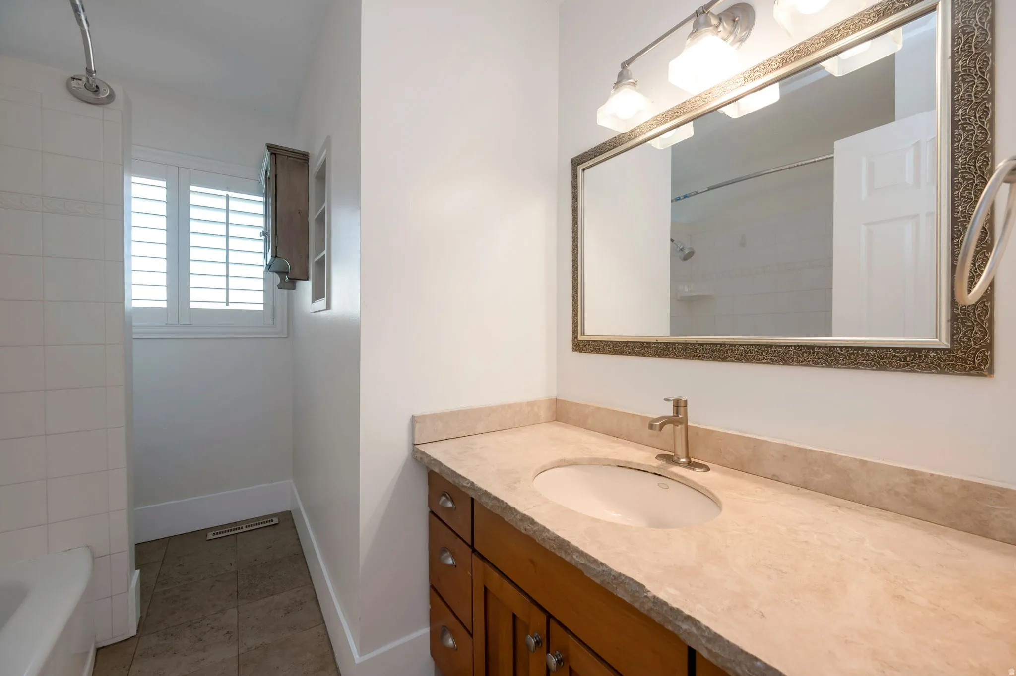 Bathroom vanity featuring a stone-finish countertop with an undermount sink, brushed nickel faucet, and an ornate framed mirror, shower tub combo