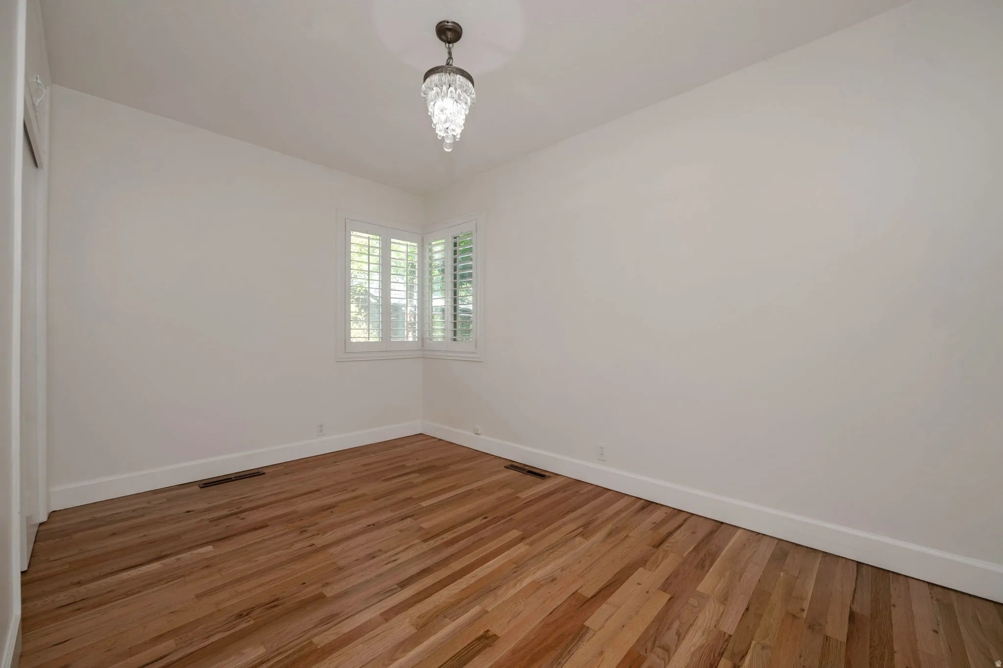 Bedroom 2 featuring wood-finish flooring, white walls, and a corner window with plantation shutters