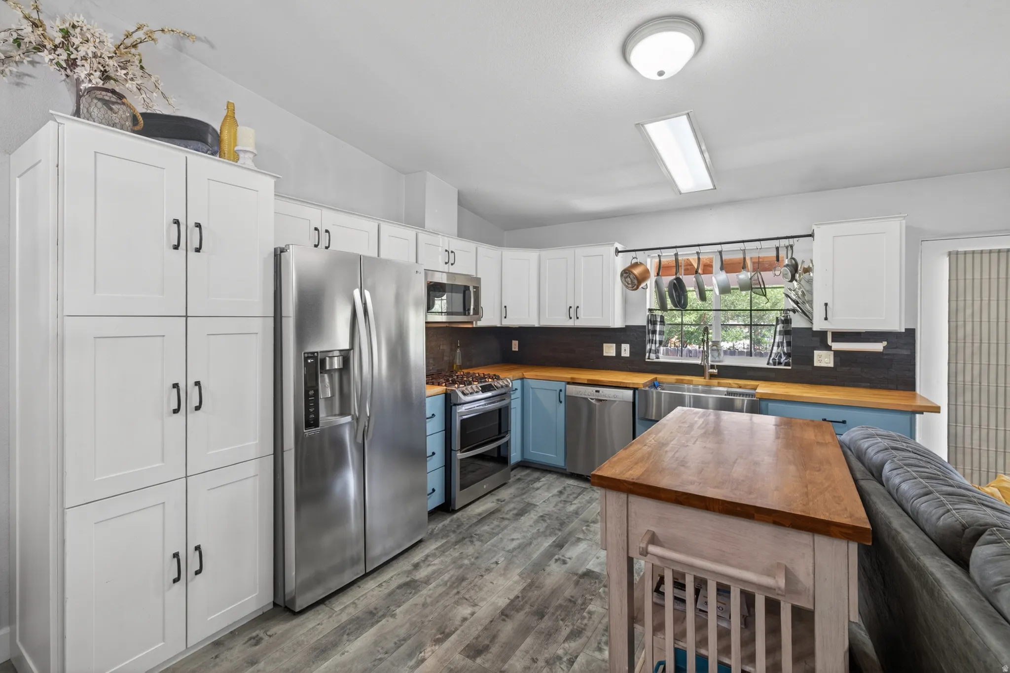 Modern kitchen featuring white upper cabinetry, blue lower cabinetry, stainless steel appliances, wood-finish countertops, and wood-finish flooring