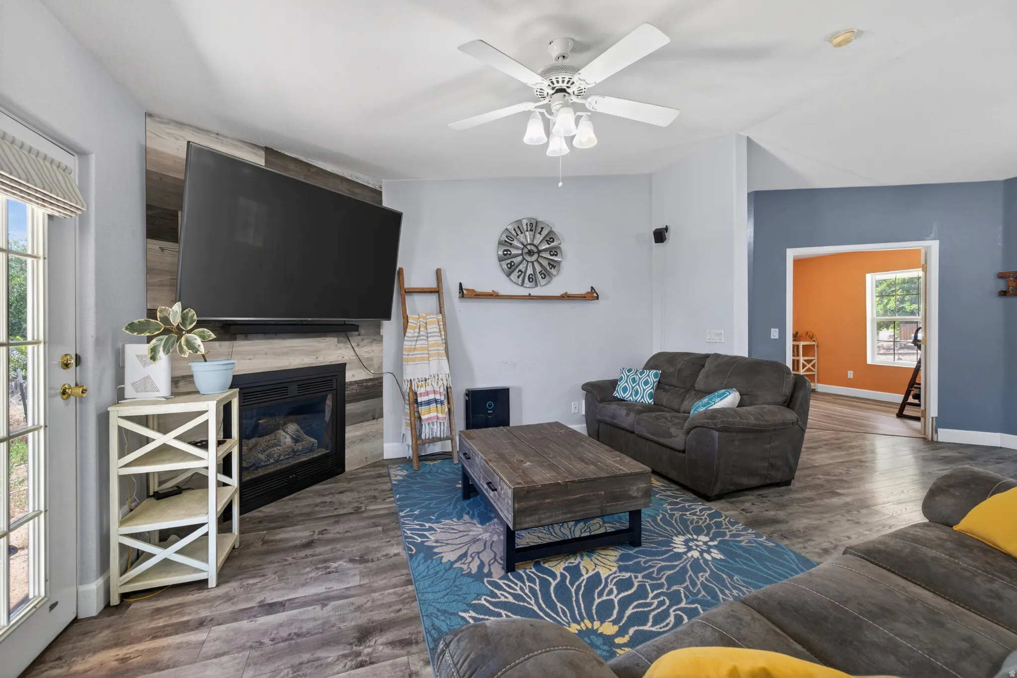 Living area with wood-finish flooring, a ceiling fan, and a fireplace featuring a wood-panel accent wall