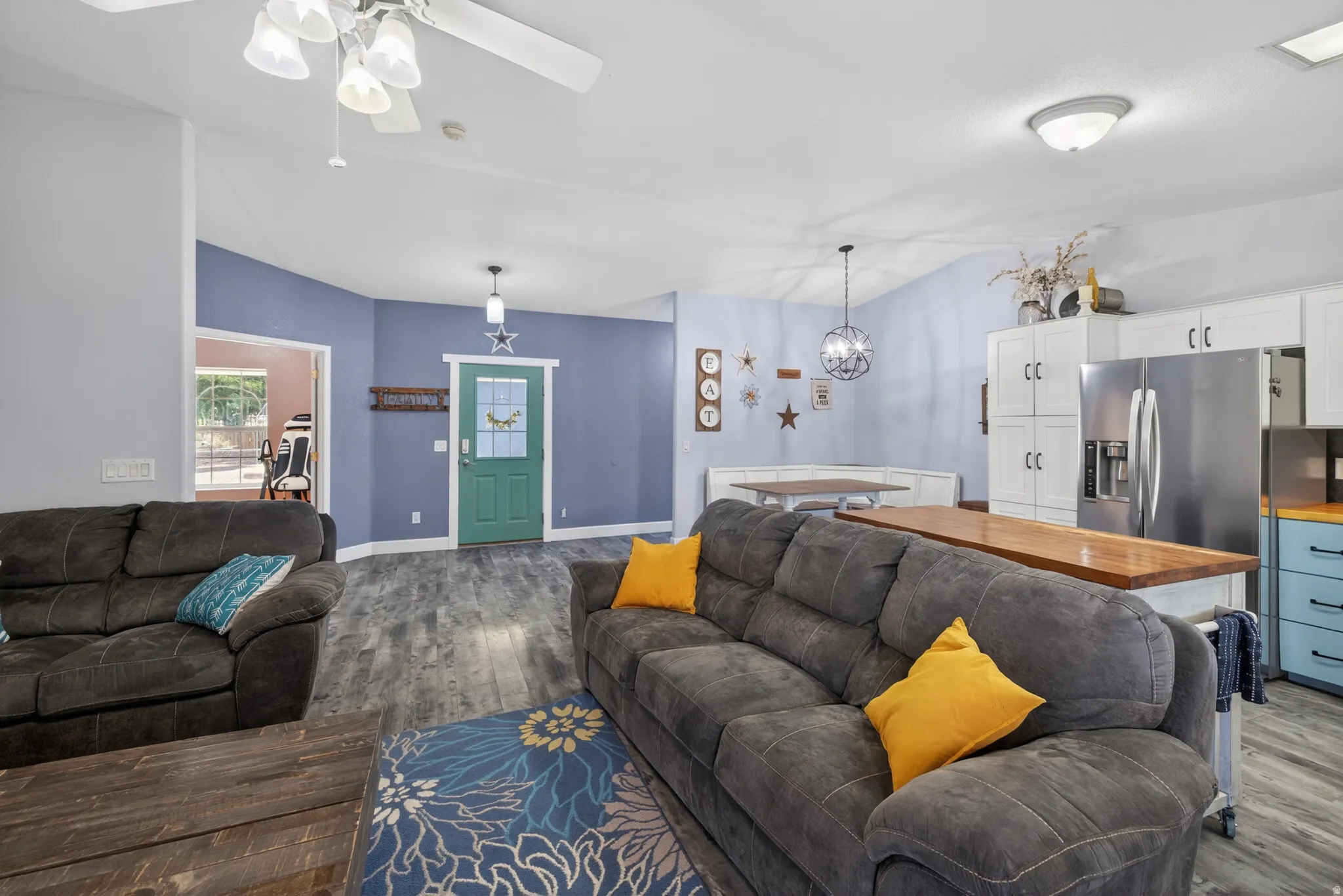 Open-concept living space featuring wood-finish flooring, vaulted ceilings, and a kitchen with stainless steel appliances, white cabinetry, and a wood countertop