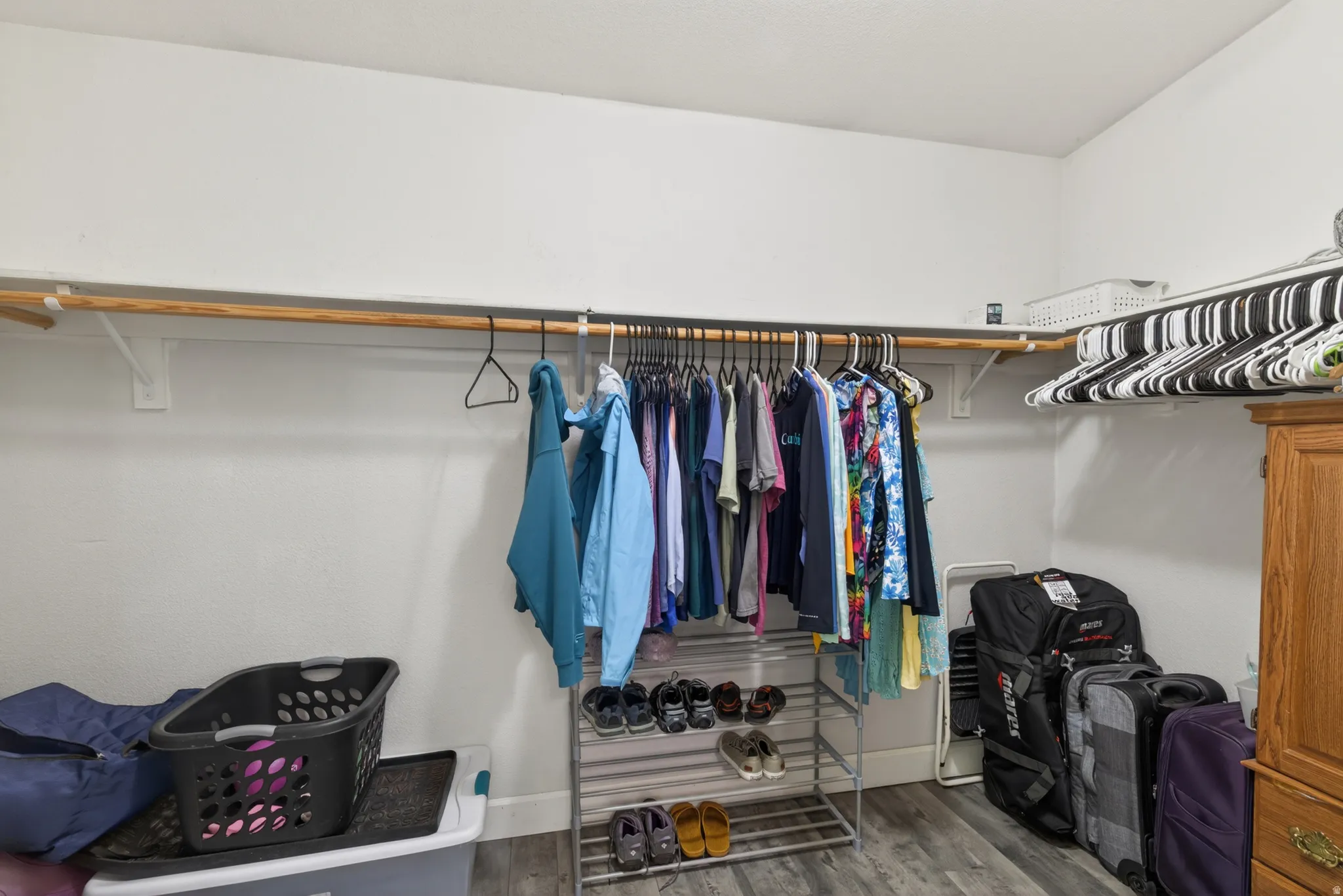 Walk-in closet featuring wood-finish flooring, two levels of hanging rods, and a white color palette