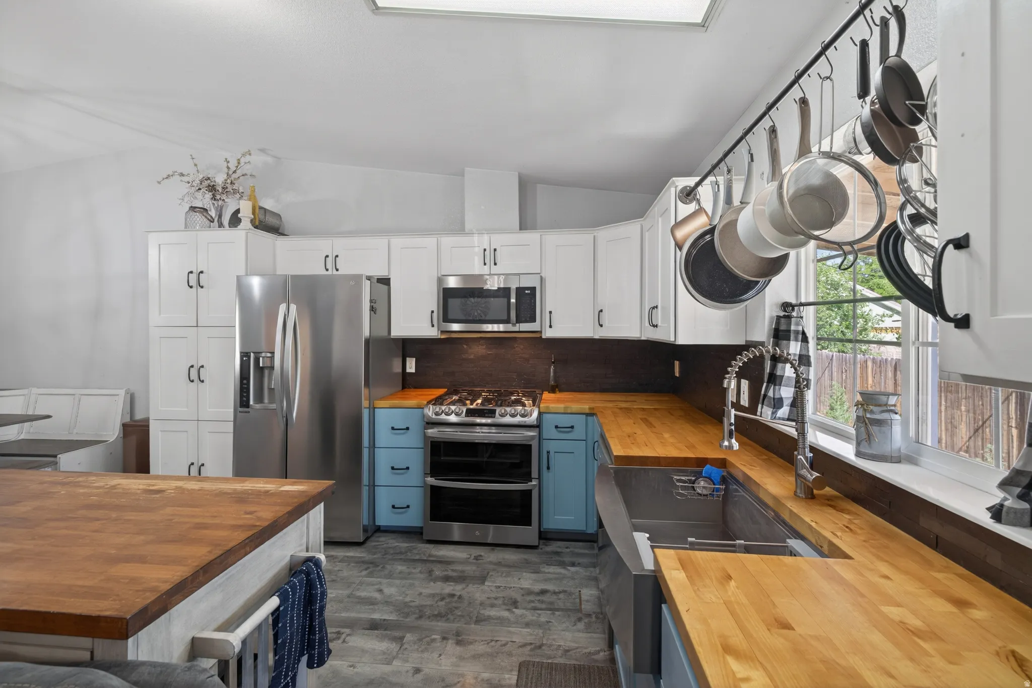 Modern kitchen featuring light wood-finish countertops, white cabinetry, stainless steel appliances, a deep basin sink with a gooseneck faucet, and light gray wood-finish flooring