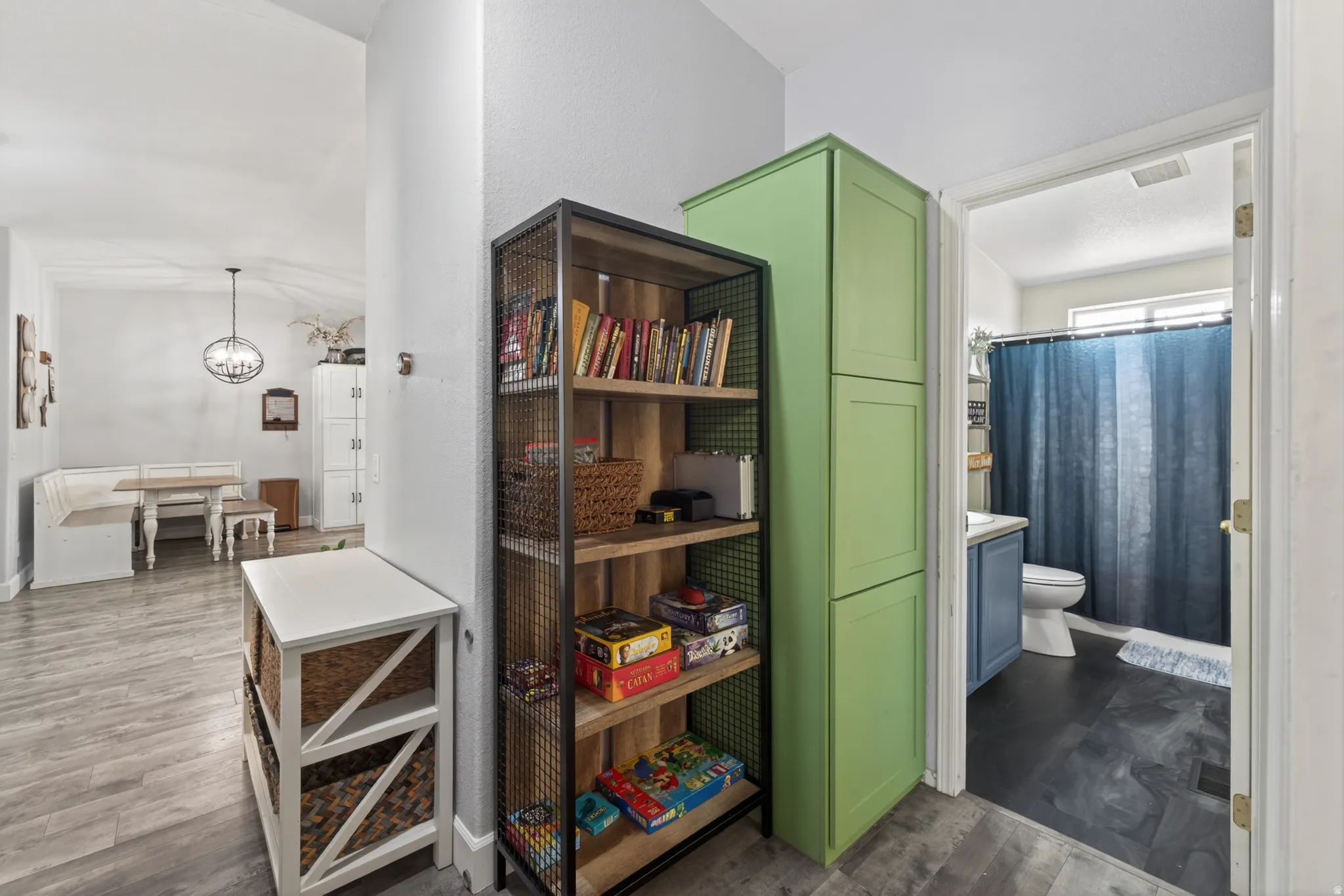 Hallway with wood-finish flooring, featuring a built-in storage unit with green cabinetry and an open-shelved metal and wood-finish bookcase