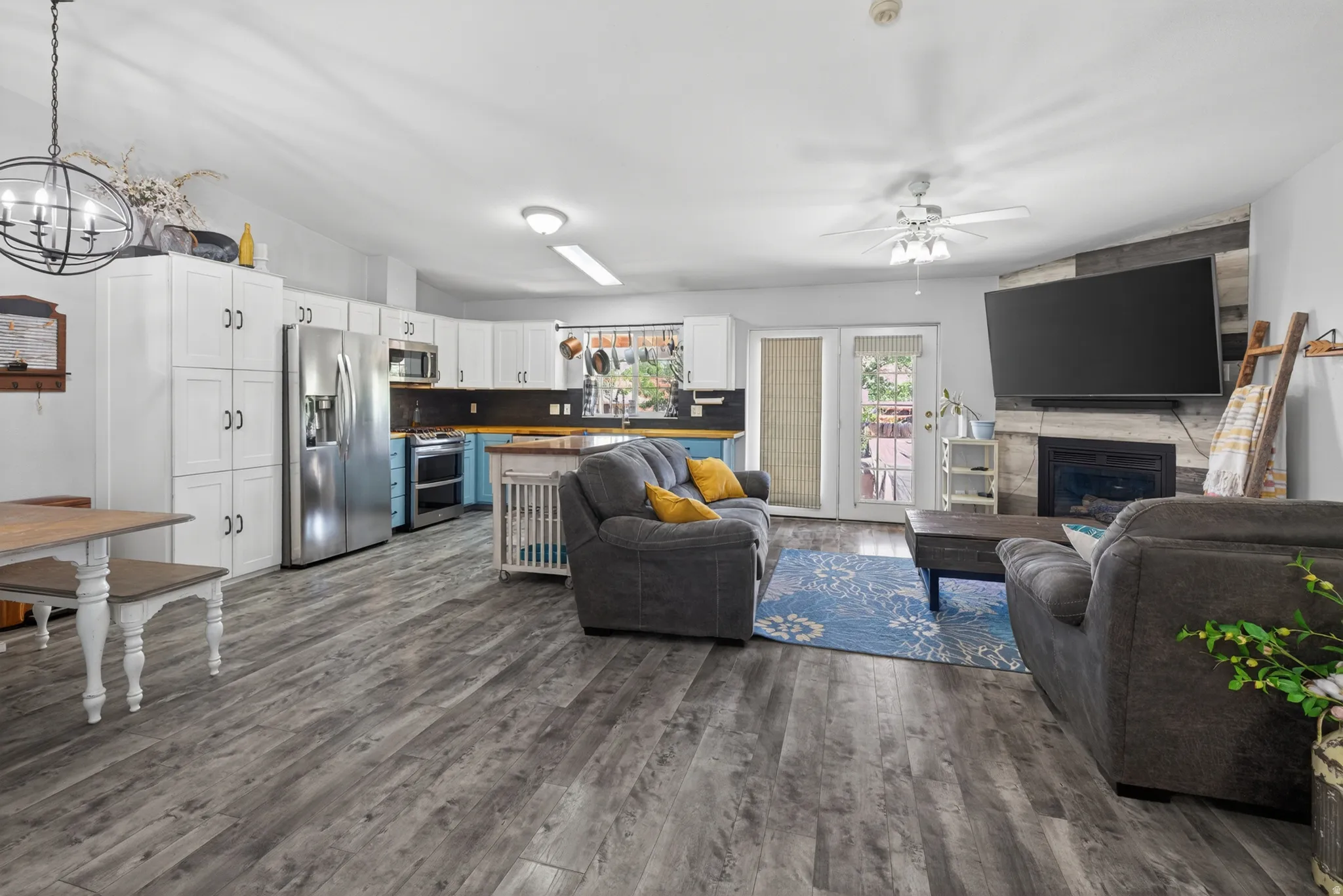 Spacious open-concept living area featuring wood-finish flooring, a corner fireplace with a shiplap accent wall, and a ceiling fan