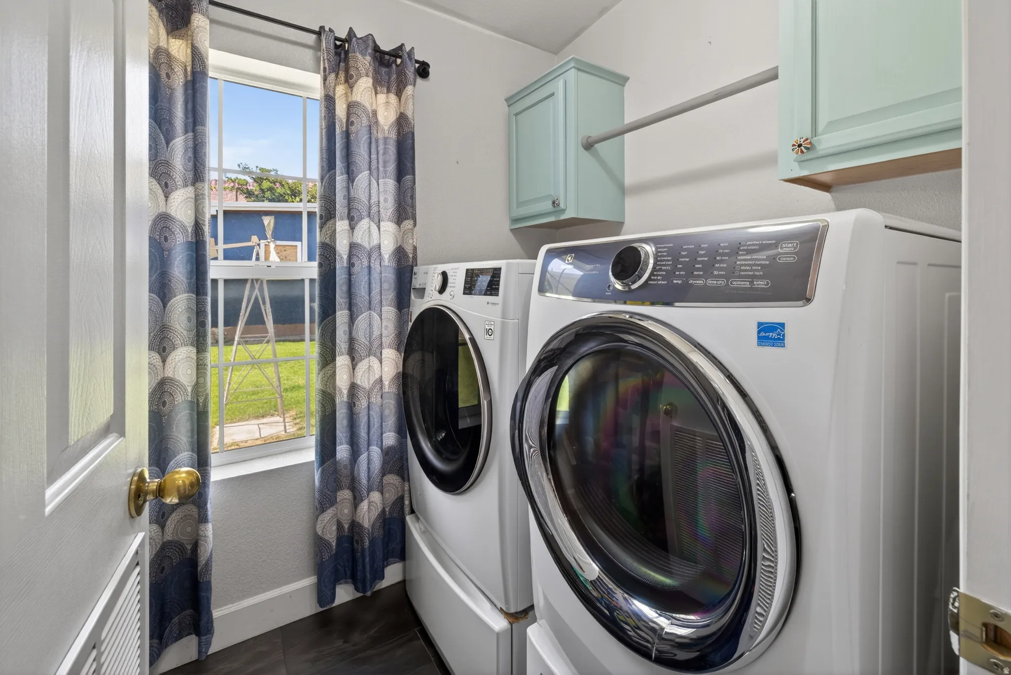 Dedicated laundry area featuring a window, wood-finish flooring, two wall-mounted cabinets, and a clothing rod