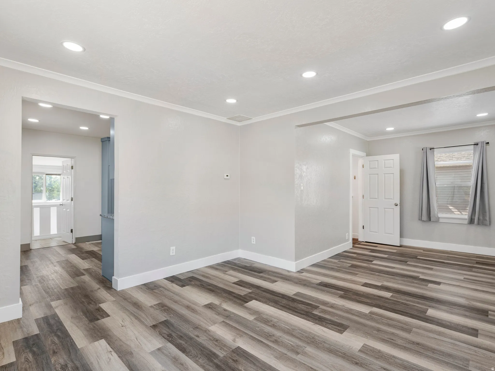 Spacious room featuring wood-finish flooring, recessed lighting, crown molding, and white baseboards