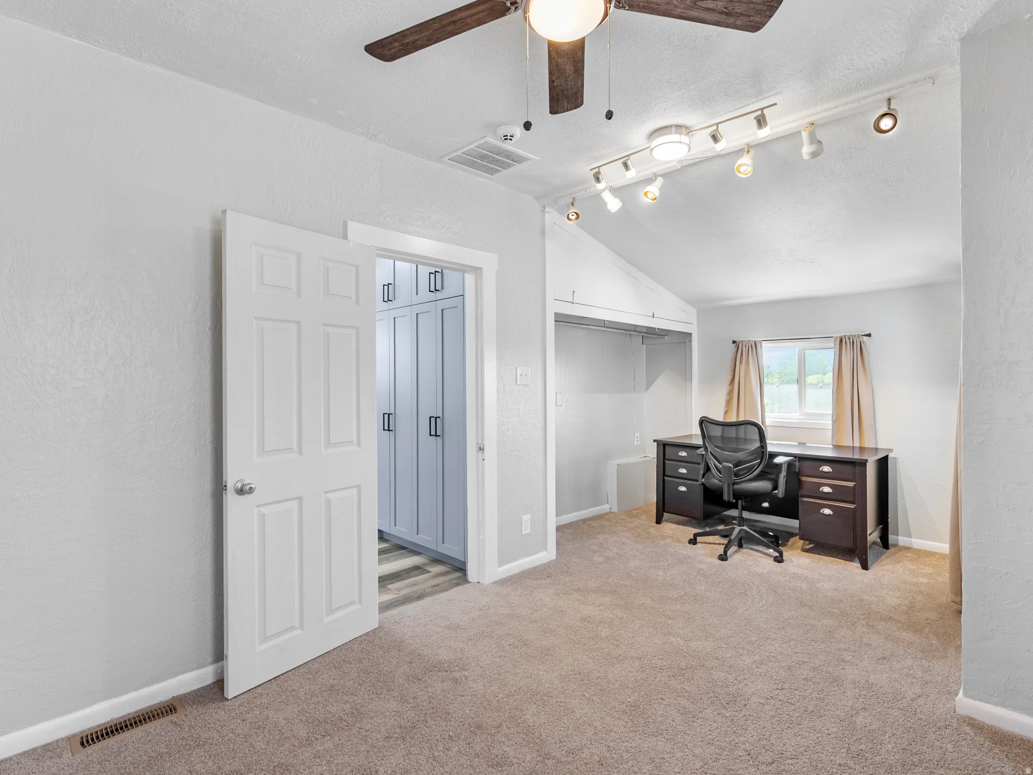 Carpeted room featuring a vaulted ceiling with track lighting and a ceiling fan