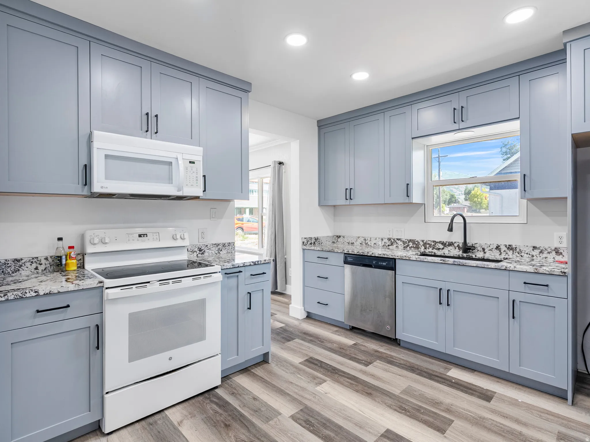 Kitchen featuring light blue cabinetry with matte black hardware, granite countertops, wood-finish flooring, and recessed lighting