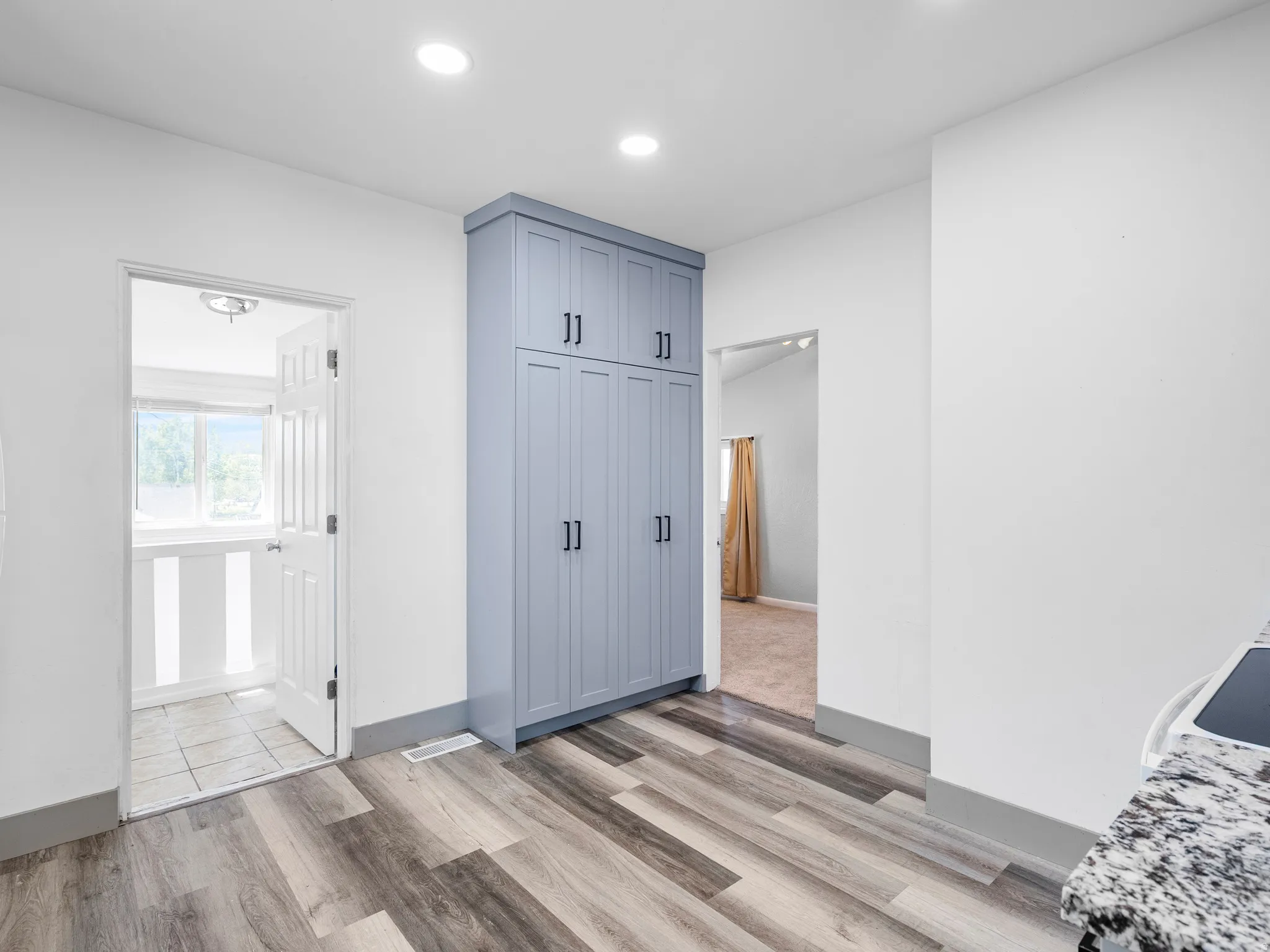 Tall built-in cabinetry with matte black hardware, wood-finish flooring, recessed lighting, and white walls