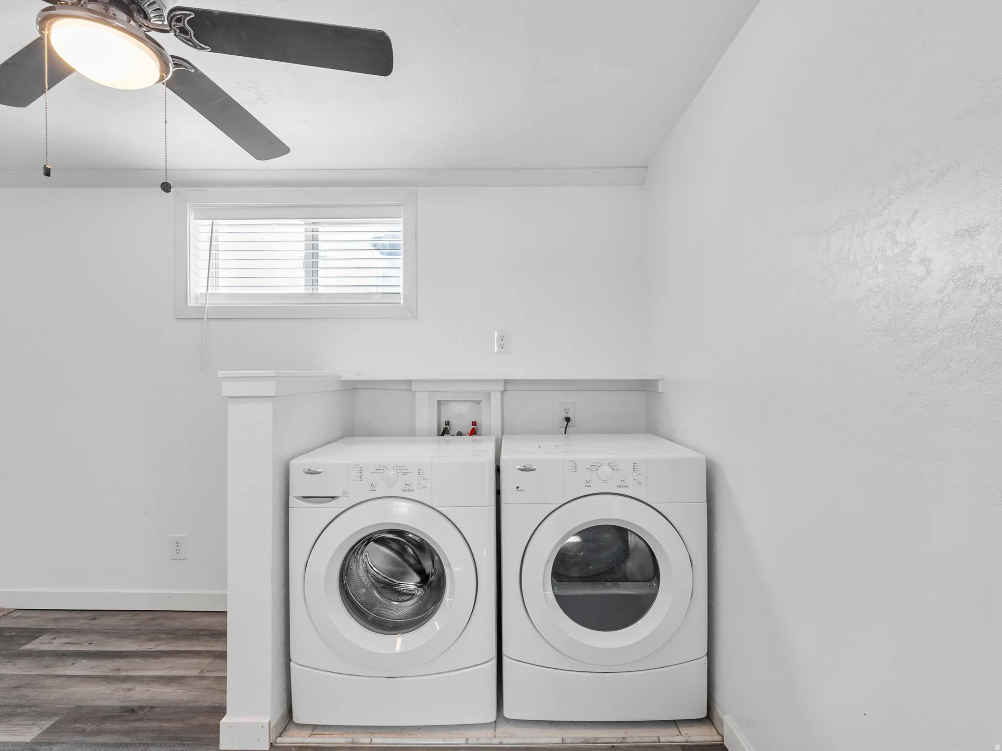 Dedicated laundry area featuring front-loading appliances, wood-finish flooring, a ceiling fan with integrated lighting, and a window with blinds
