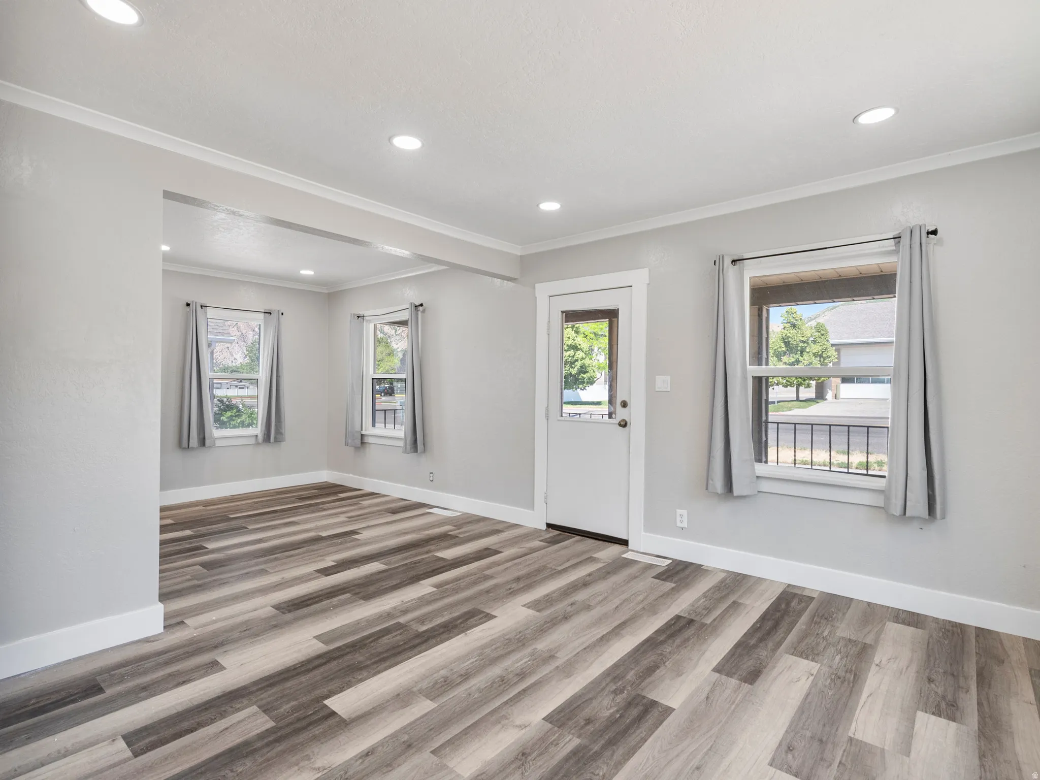 Open-concept living space with multi-toned wood-finish flooring, recessed lighting, white baseboards, and crown molding