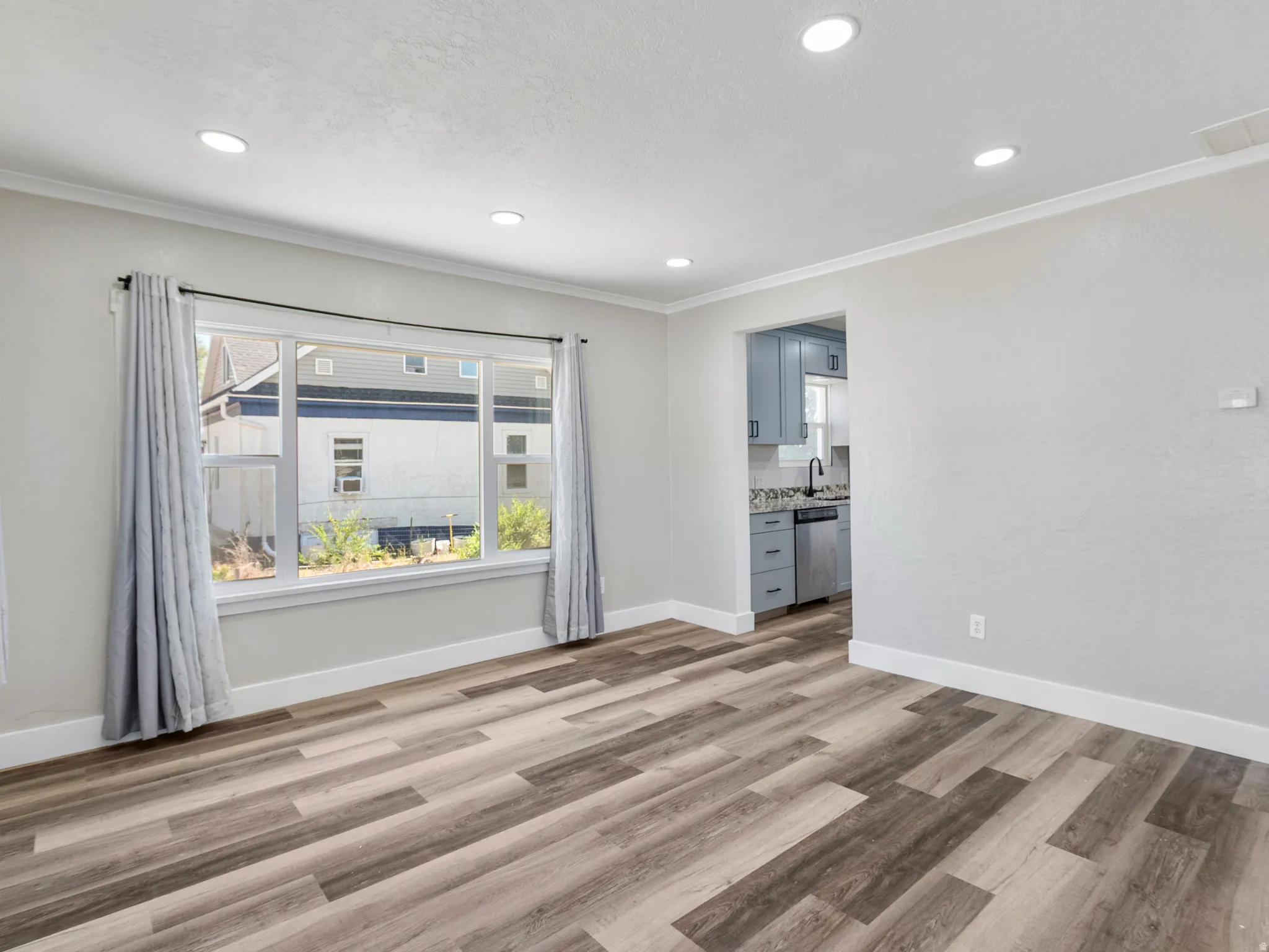 Spacious living area featuring wood-finish flooring, recessed lighting, and a wide window with white trim