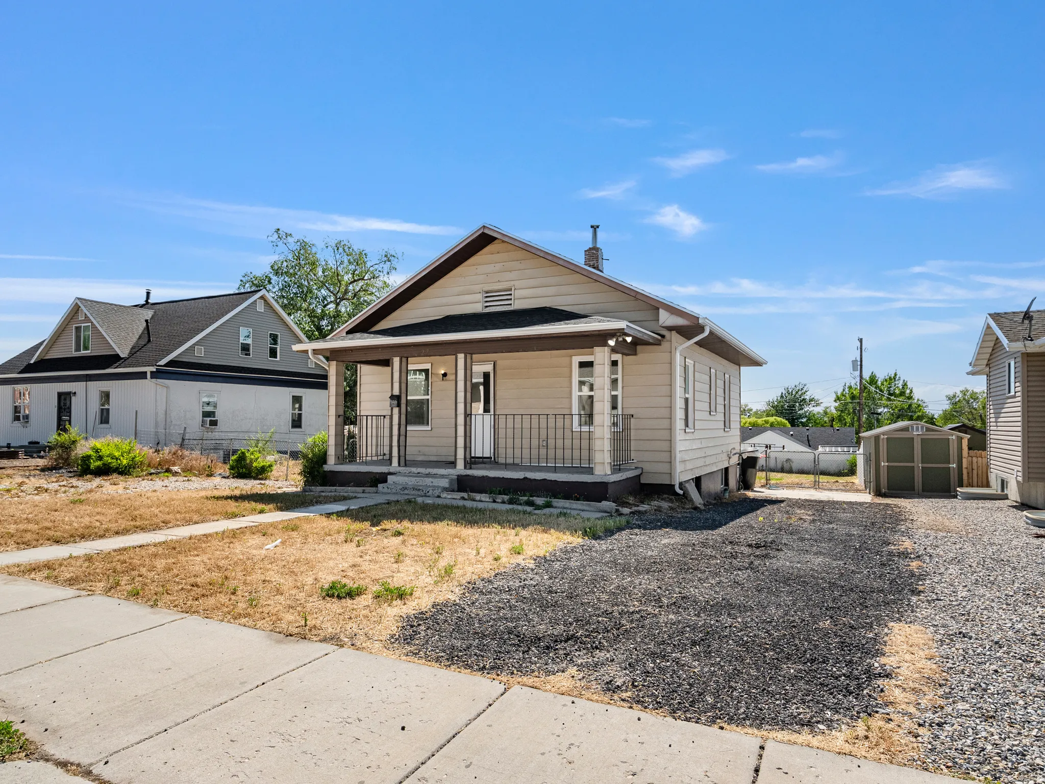 Single-story residence featuring light-toned siding, a covered front porch with dark railings, and a gravel driveway