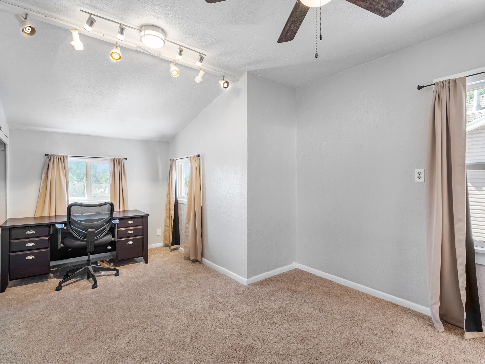 Room featuring vaulted ceiling, track lighting, ceiling fan, and neutral carpet flooring