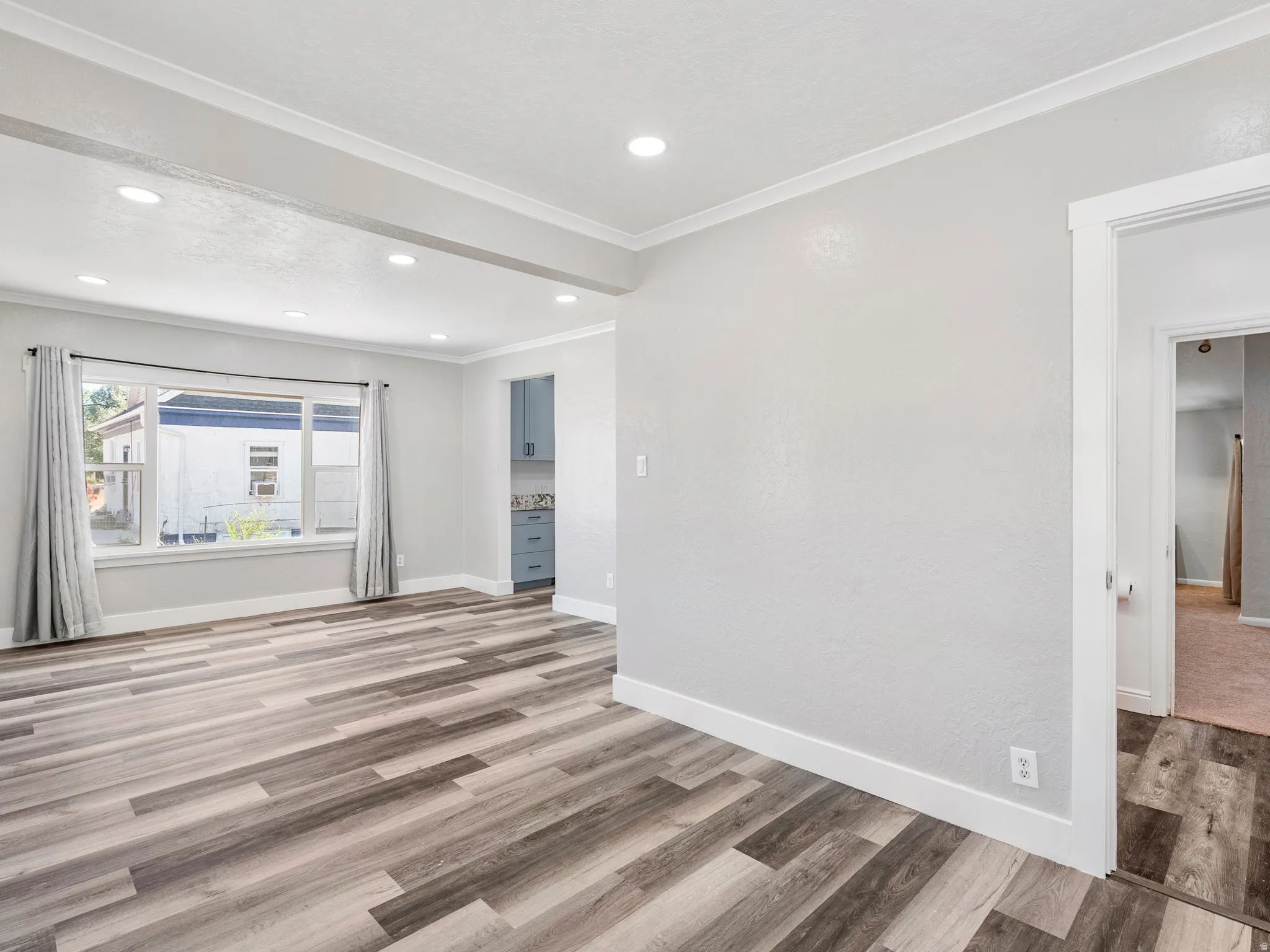 Spacious room featuring wood-finish flooring, recessed lighting, and a large window with window treatments