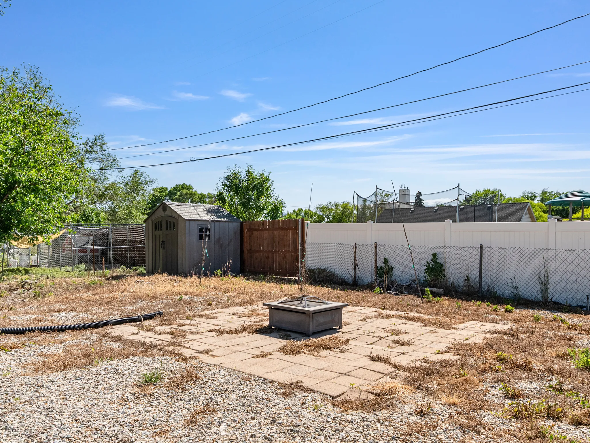 Paved patio area with a central fire pit, bordered by a gravel section and a storage shed