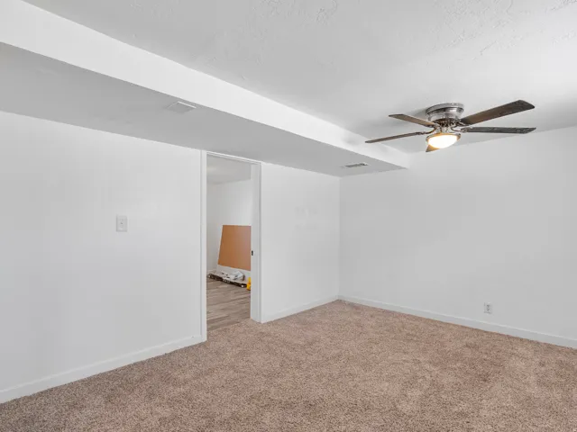 Carpeted room with white walls, a ceiling fan with integrated lighting, and an open doorway leading to a space with wood-finish flooring