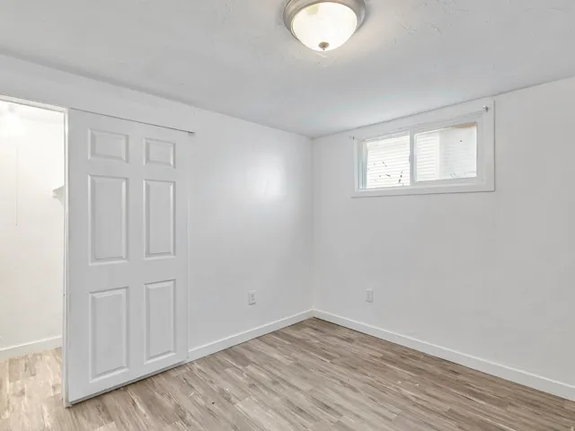 Room featuring wood-finish flooring, white walls, a single window with blinds, a ceiling-mounted light fixture, and a white paneled sliding barn door