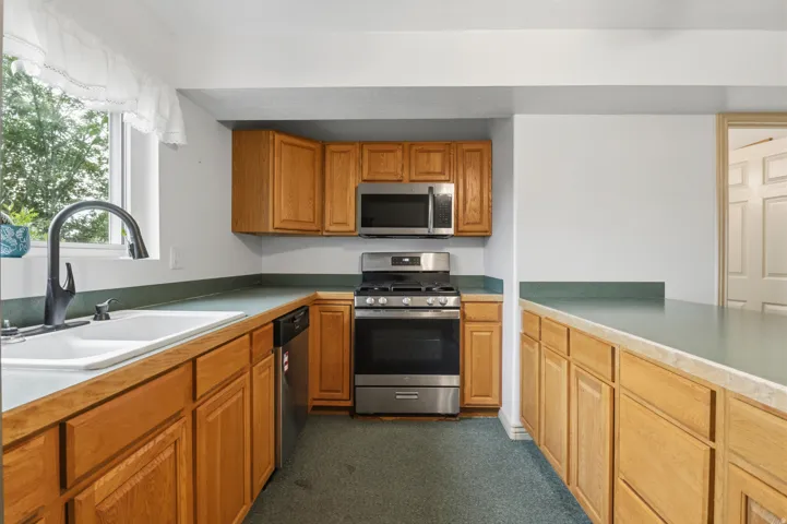 Kitchen featuring natural wood cabinetry, light green countertops, stainless steel appliances, and a window above the sink