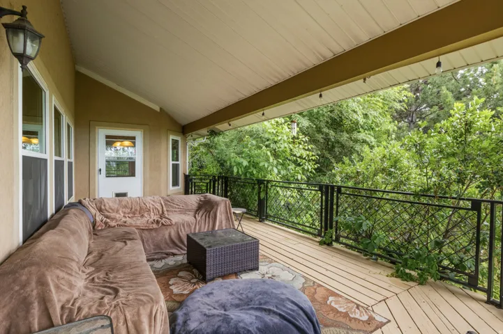 Covered outdoor deck featuring natural wood flooring and a black metal railing