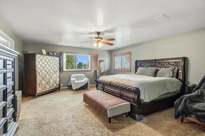 Carpeted bedroom featuring a ceiling fan, a window with plantation shutters, and a sloped ceiling