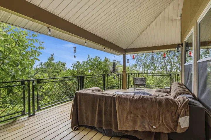 Covered outdoor deck with light wood-finish flooring, featuring a black metal railing